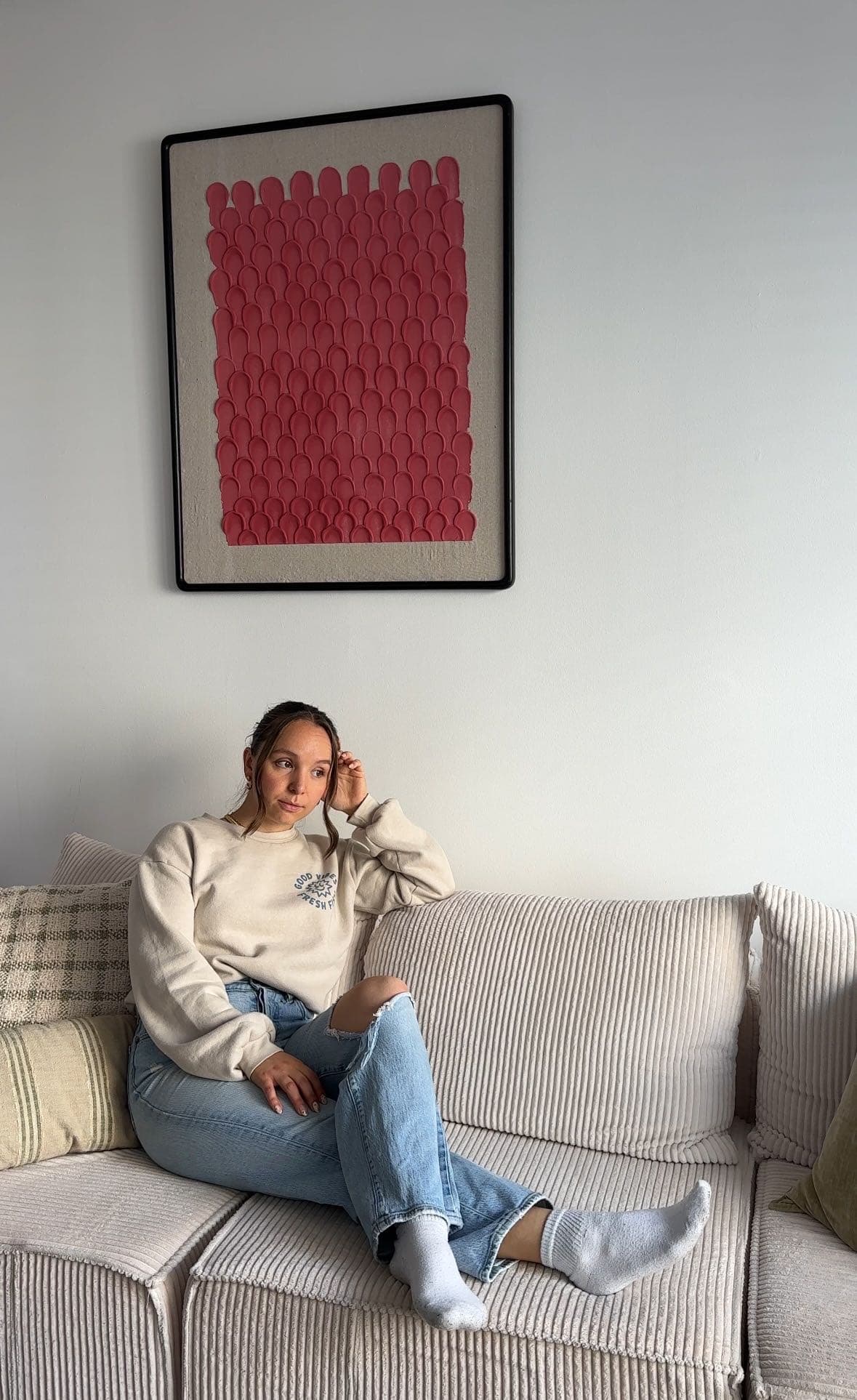 Bridget on a couch in her apartment with DIY textured art above on wall